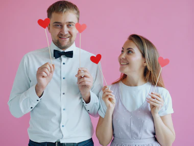 Couple posing with heart props against a pink backdrop