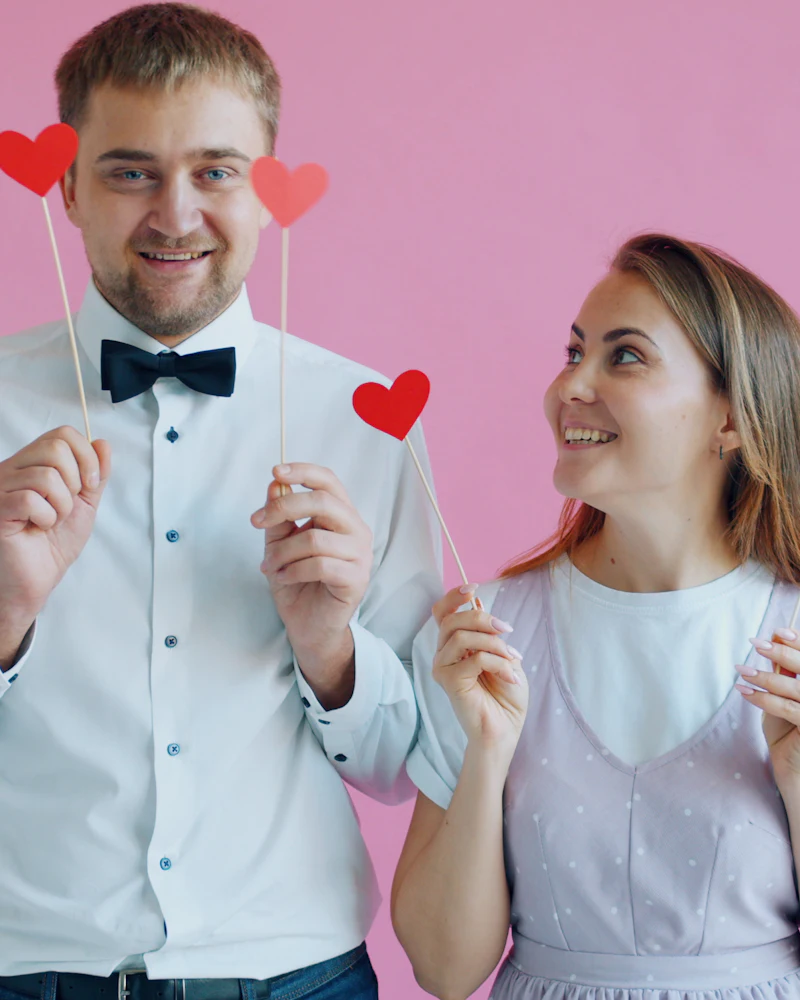 Pareja posando con corazones de atrezo sobre fondo rosa