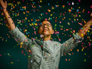 Man with arms raised amid colourful confetti